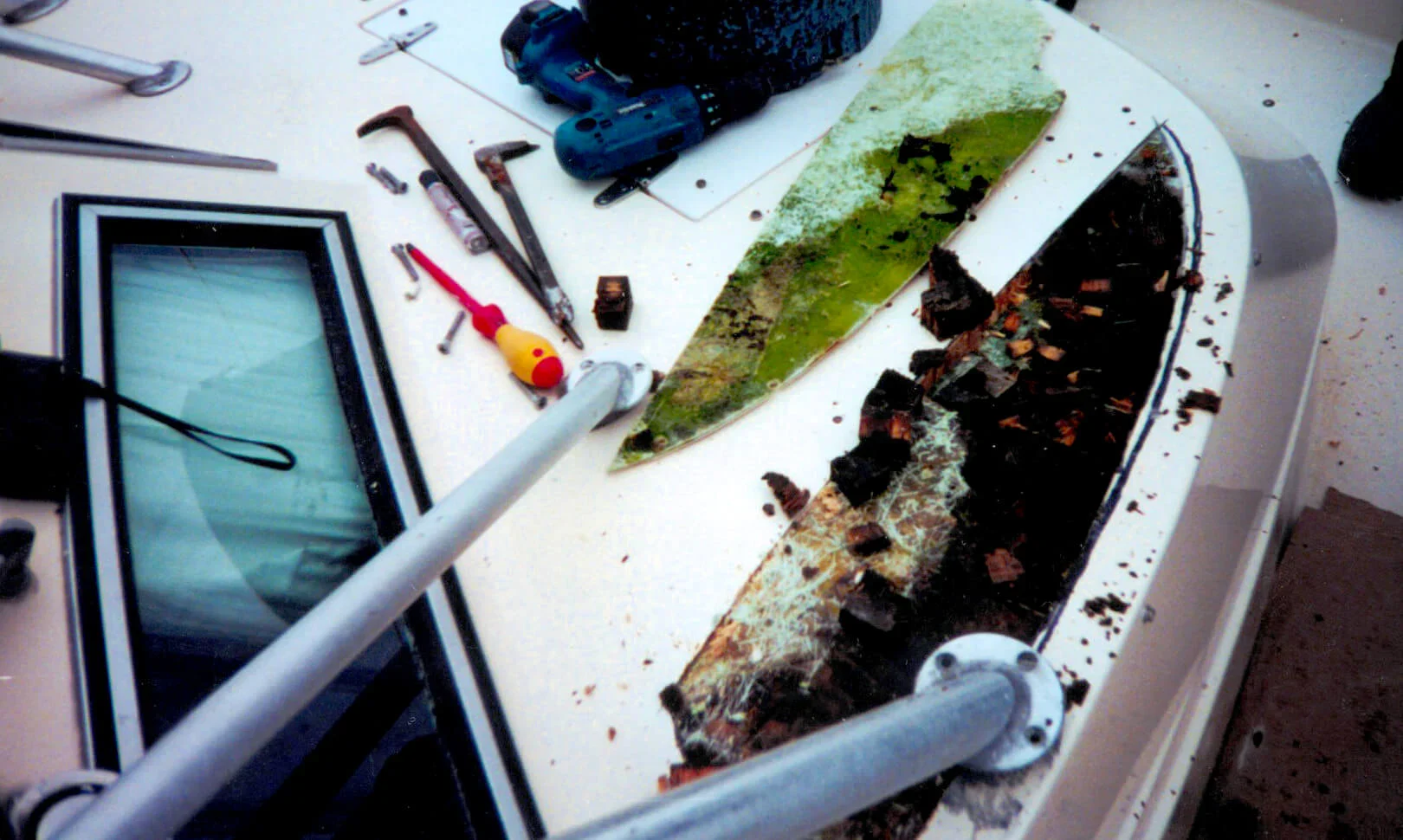 Tools and a partially removed layer of a boat's surface, revealing wood debris and green algae on a workbench.