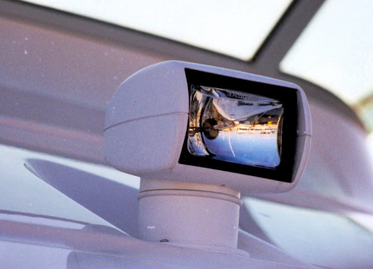 Close-up of a white spotlight mounted on a vehicle, reflecting surrounding scenery.