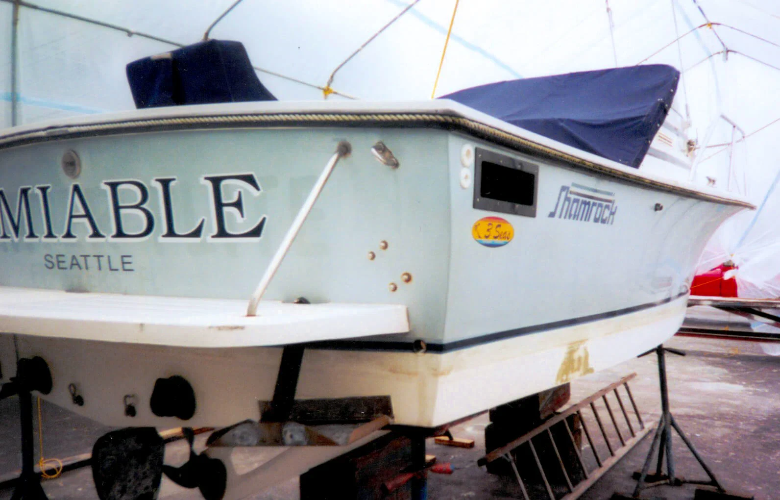 A blue boat named Miable from Seattle is on a trailer, partially covered, with the word Shamrock visible on its side.